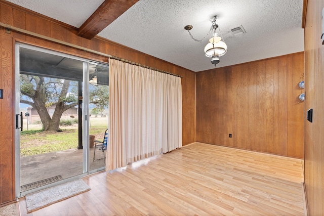 unfurnished room with wooden walls, visible vents, wood finished floors, beamed ceiling, and a textured ceiling