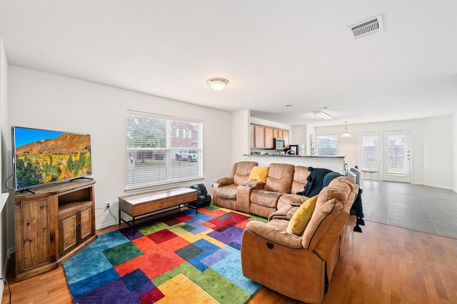 living room featuring baseboards, a healthy amount of sunlight, visible vents, and light wood-style floors