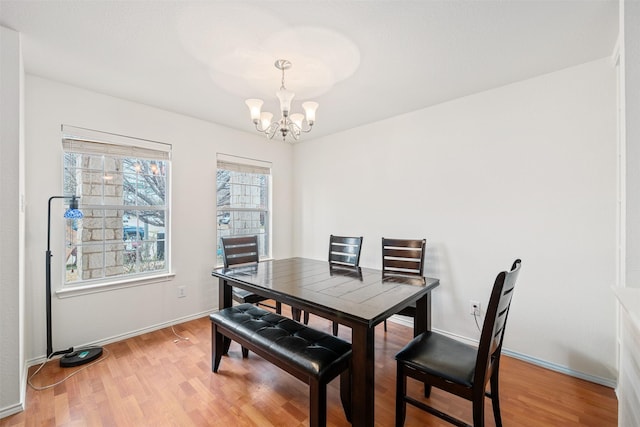 dining area featuring light wood-style floors, a notable chandelier, and baseboards