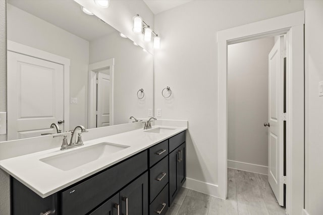 full bath with double vanity, baseboards, a sink, and wood finished floors