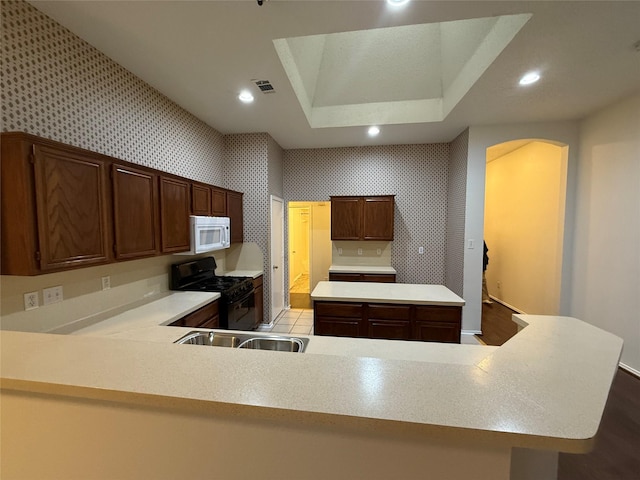 kitchen with white microwave, black gas range, a kitchen island, visible vents, and light countertops