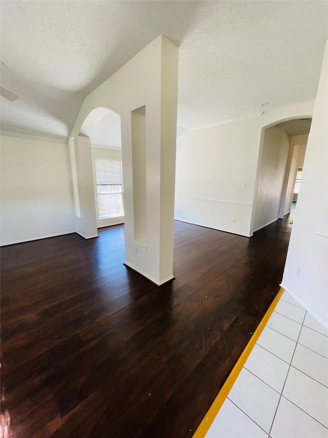 spare room with lofted ceiling, arched walkways, a textured ceiling, and wood finished floors