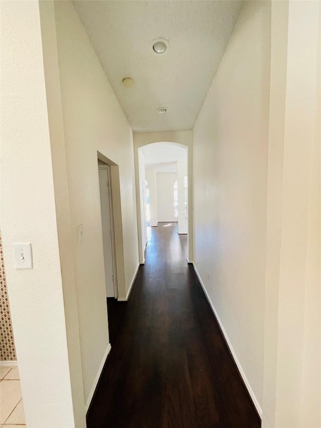 hall featuring arched walkways, baseboards, and wood finished floors