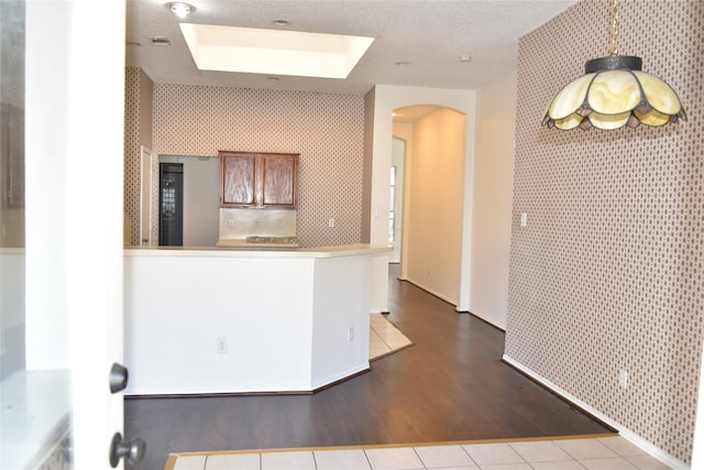 kitchen with an accent wall, arched walkways, brown cabinets, and wallpapered walls