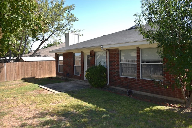 rear view of property with a chimney, fence, a lawn, and brick siding