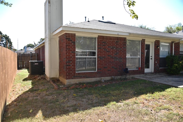 exterior space featuring brick siding, a patio, central AC, fence, and a front lawn