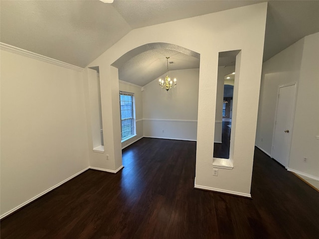 empty room featuring baseboards, arched walkways, wood finished floors, vaulted ceiling, and a chandelier