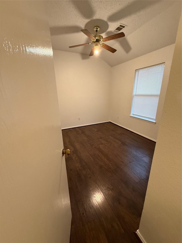 empty room featuring a textured ceiling, dark wood finished floors, visible vents, and a ceiling fan