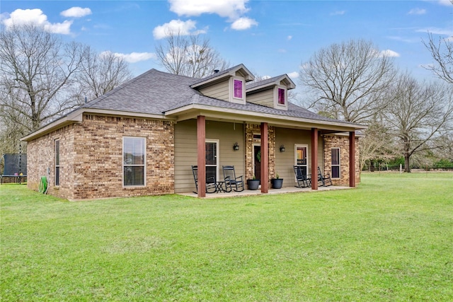 view of front of house with roof with shingles, brick siding, a front lawn, and a patio area