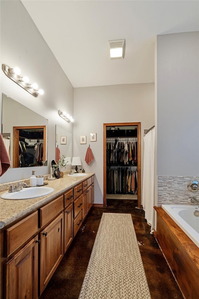 full bathroom featuring double vanity, a spacious closet, a sink, and a bath