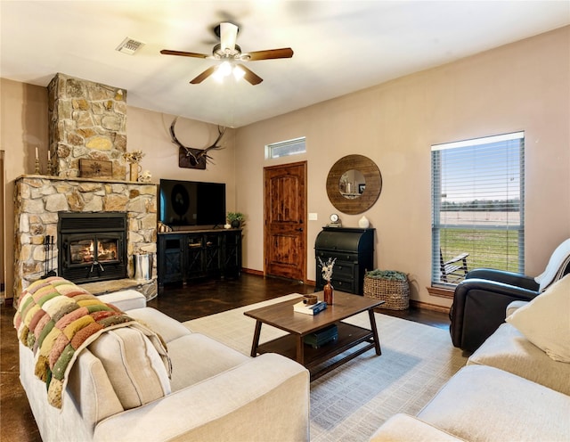 living room with visible vents, ceiling fan, a stone fireplace, wood finished floors, and baseboards