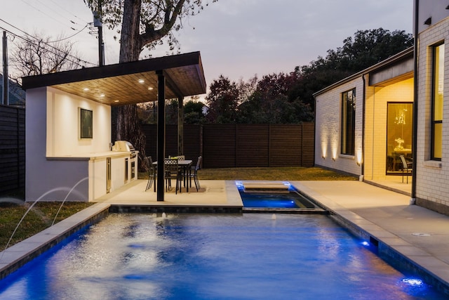 pool at dusk featuring fence, exterior kitchen, a patio area, an outdoor pool, and an in ground hot tub