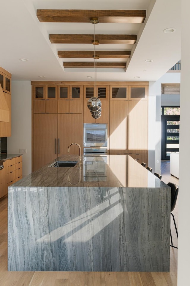 kitchen with dark stone counters, oven, a sink, beamed ceiling, and modern cabinets