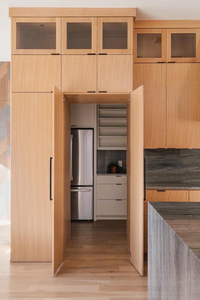 kitchen featuring light wood finished floors, light brown cabinets, glass insert cabinets, freestanding refrigerator, and modern cabinets