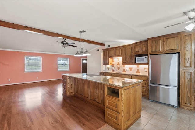 kitchen with white microwave, a ceiling fan, freestanding refrigerator, a kitchen island, and a sink