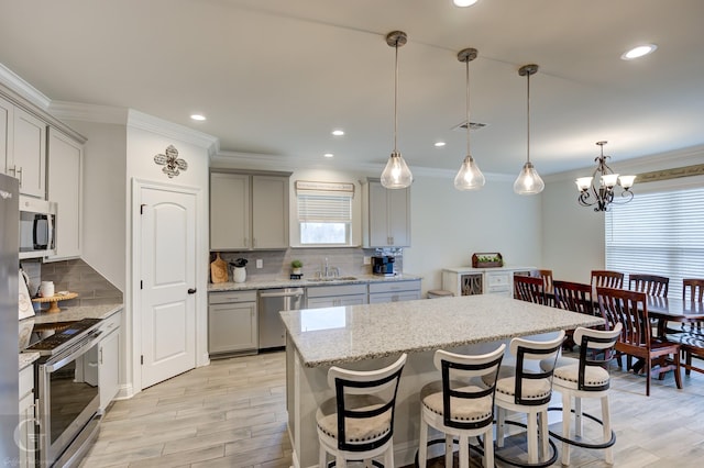 kitchen with appliances with stainless steel finishes, gray cabinets, light wood-style flooring, and a kitchen bar