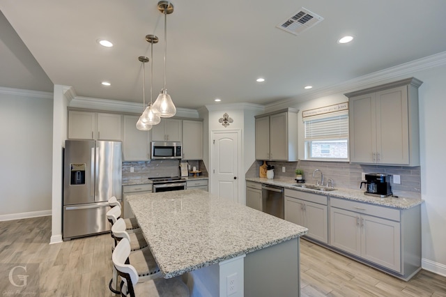 kitchen featuring stainless steel appliances, a sink, visible vents, gray cabinets, and a kitchen bar