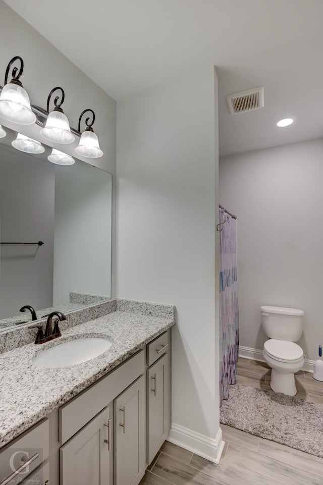 bathroom with visible vents, toilet, vanity, wood finished floors, and baseboards