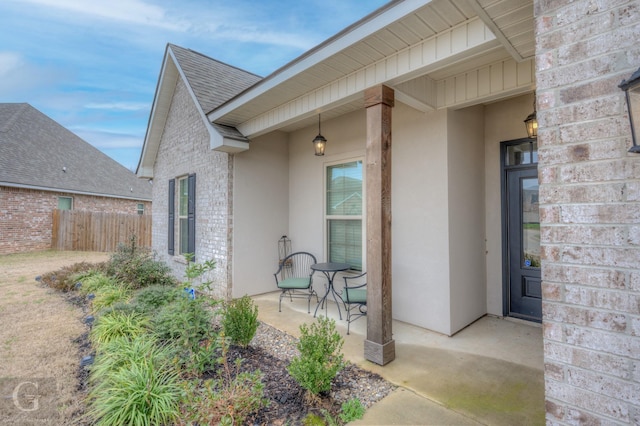 doorway to property featuring brick siding, roof with shingles, fence, and stucco siding