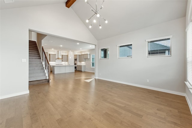 unfurnished living room featuring high vaulted ceiling, stairs, light wood-type flooring, beamed ceiling, and an inviting chandelier