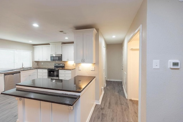 kitchen featuring dark countertops, decorative backsplash, appliances with stainless steel finishes, light wood-style floors, and white cabinetry