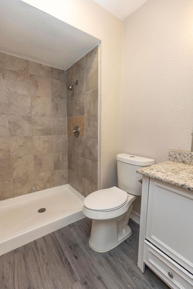 bathroom with a tile shower, vanity, toilet, and wood finished floors