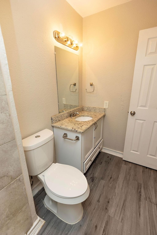 bathroom with toilet, baseboards, wood finished floors, and vanity