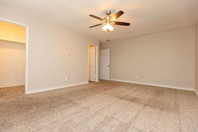 unfurnished bedroom featuring a walk in closet, light colored carpet, visible vents, a ceiling fan, and baseboards