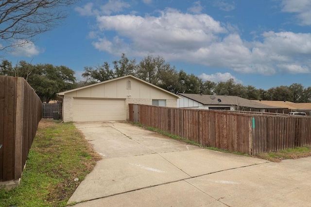 view of side of property with a garage, driveway, fence private yard, board and batten siding, and brick siding