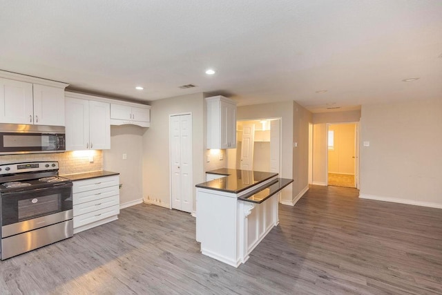 kitchen featuring dark countertops, white cabinets, stainless steel appliances, and wood finished floors