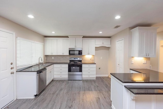 kitchen featuring visible vents, dark countertops, stainless steel appliances, light wood-type flooring, and a sink