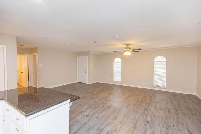 interior space with baseboards, a ceiling fan, dark stone countertops, light wood-style floors, and white cabinetry