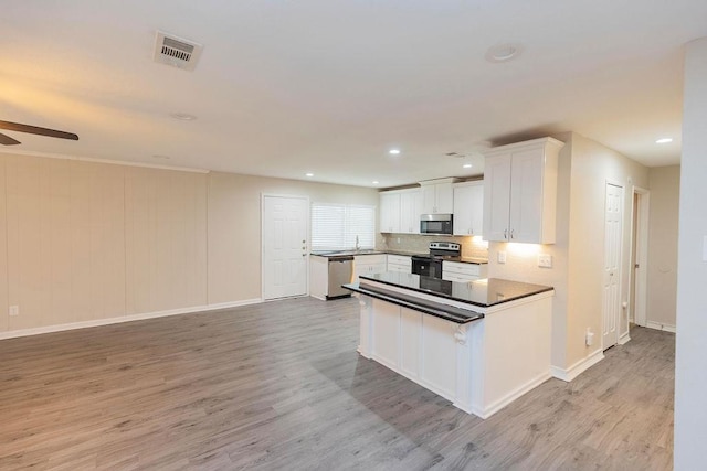 kitchen featuring appliances with stainless steel finishes, white cabinetry, light wood-style floors, and backsplash