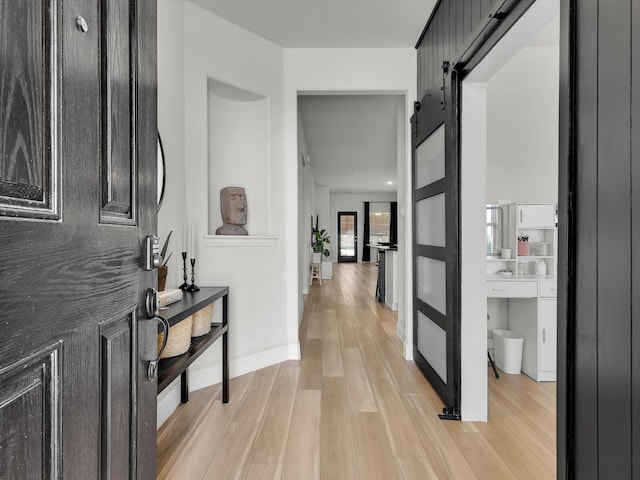 hallway featuring baseboards, light wood finished floors, and a barn door