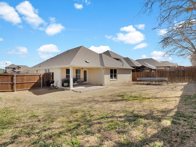 back of property with a trampoline, a patio area, a fenced backyard, and brick siding