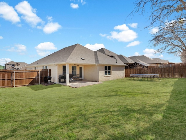 rear view of property with a trampoline, brick siding, a lawn, a patio area, and a fenced backyard