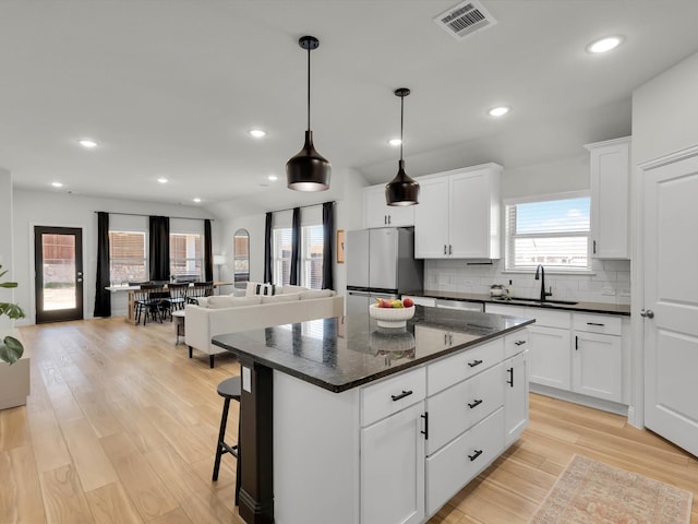 kitchen with visible vents, backsplash, freestanding refrigerator, open floor plan, and a sink