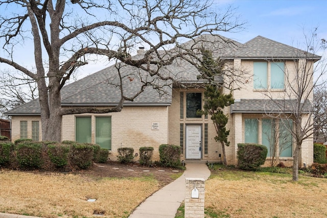 view of front of home featuring brick siding, roof with shingles, a chimney, and a front lawn