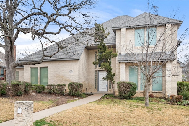 view of front of home with roof with shingles, brick siding, and a front lawn