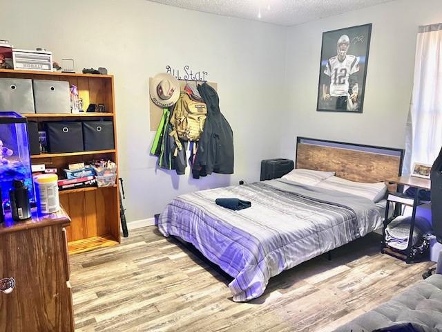 bedroom featuring a textured ceiling, baseboards, and wood finished floors