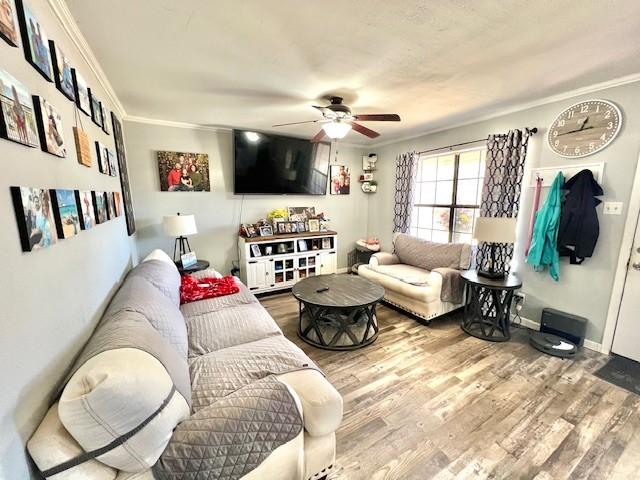 living area featuring crown molding, baseboards, ceiling fan, and wood finished floors