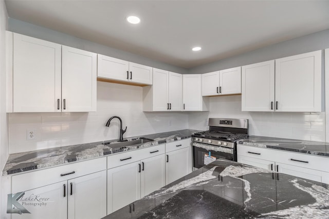 kitchen with a sink, dark stone counters, stainless steel range with gas cooktop, and white cabinetry