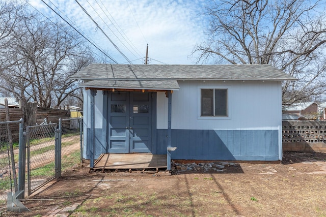 exterior space with an outbuilding, roof with shingles, fence, and a gate