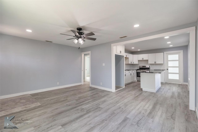 kitchen with visible vents, open floor plan, stainless steel stove, light wood-type flooring, and white cabinetry