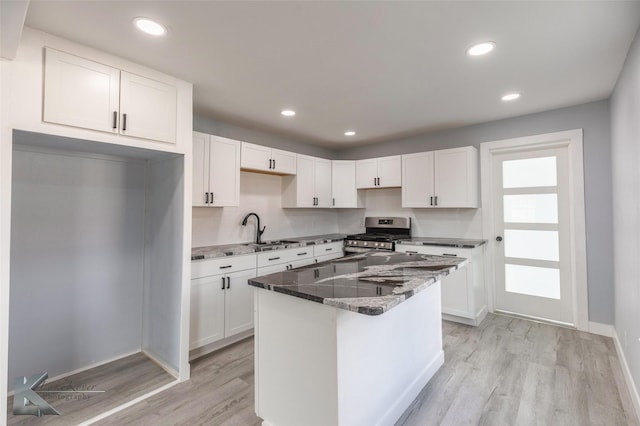 kitchen with light wood finished floors, stainless steel gas range oven, stone countertops, white cabinets, and a sink