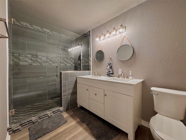 full bath with a textured wall, a sink, toilet, and wood finished floors