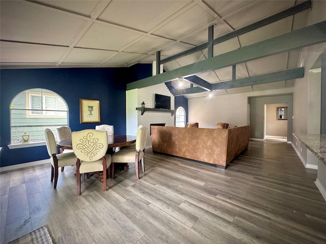 dining area featuring vaulted ceiling with beams, a fireplace, wood finished floors, and a healthy amount of sunlight