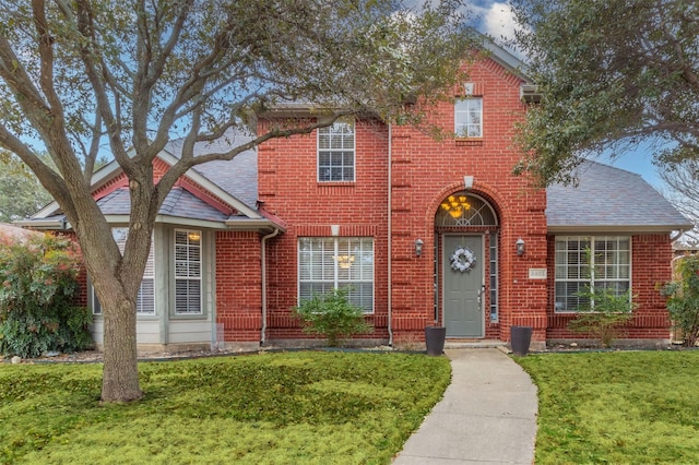 traditional-style home featuring a front yard, brick siding, and roof with shingles