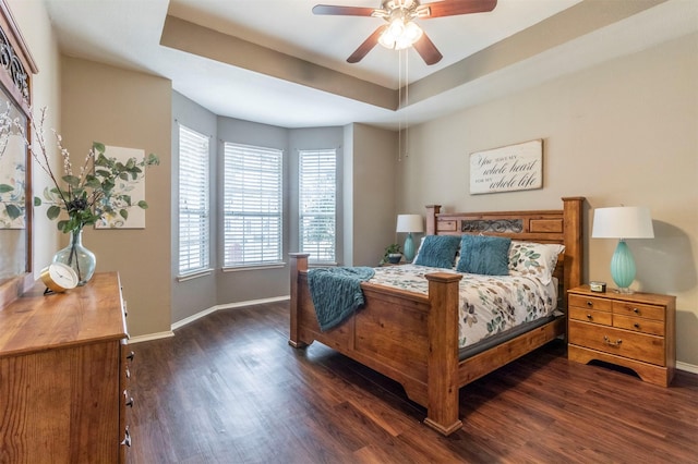 bedroom featuring dark wood finished floors, ceiling fan, baseboards, and a tray ceiling