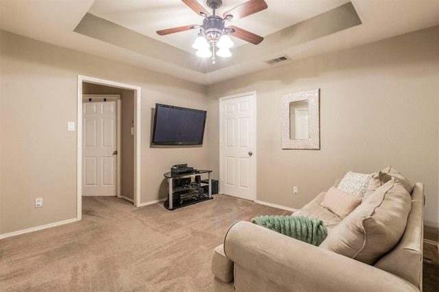 living room featuring a tray ceiling, carpet, baseboards, and visible vents